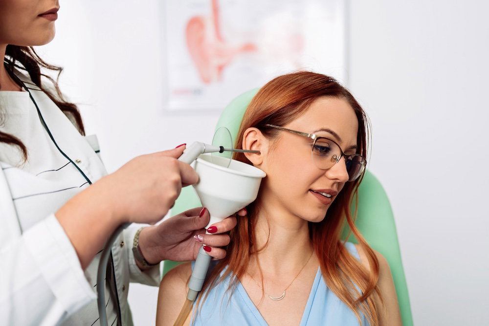 Otolaryngologist doing ear irrigation and earwax removal to a young adult woman with modern medical equipment. Healthcare and medicine concept.
