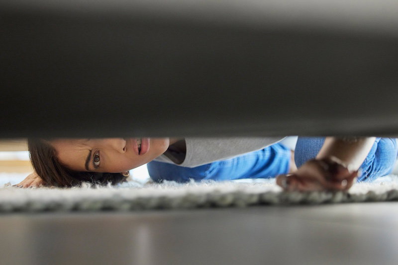 Woman checking under furniture after losing a hearing aid at home